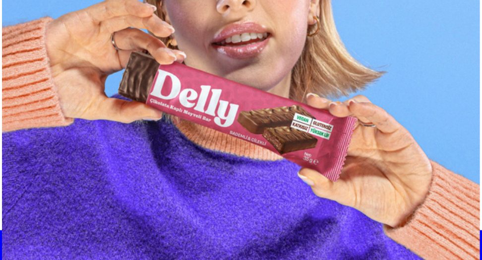 Model in violet knit holding a Delly bar